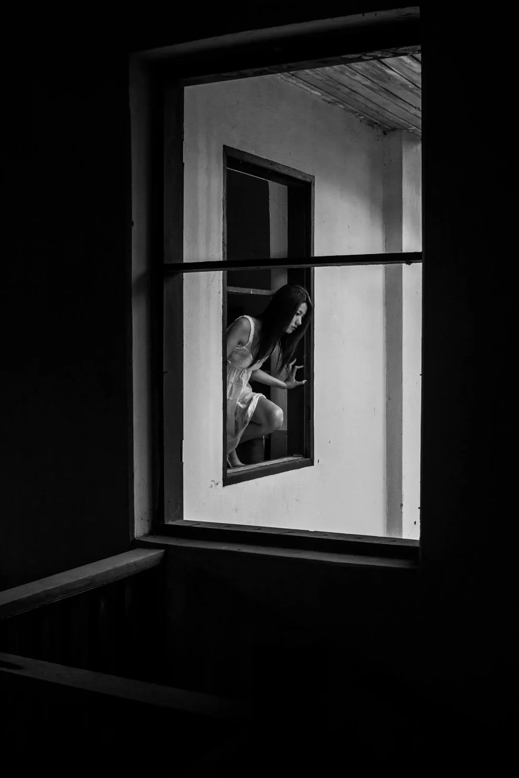 A figure seen through a window frame in a dark room